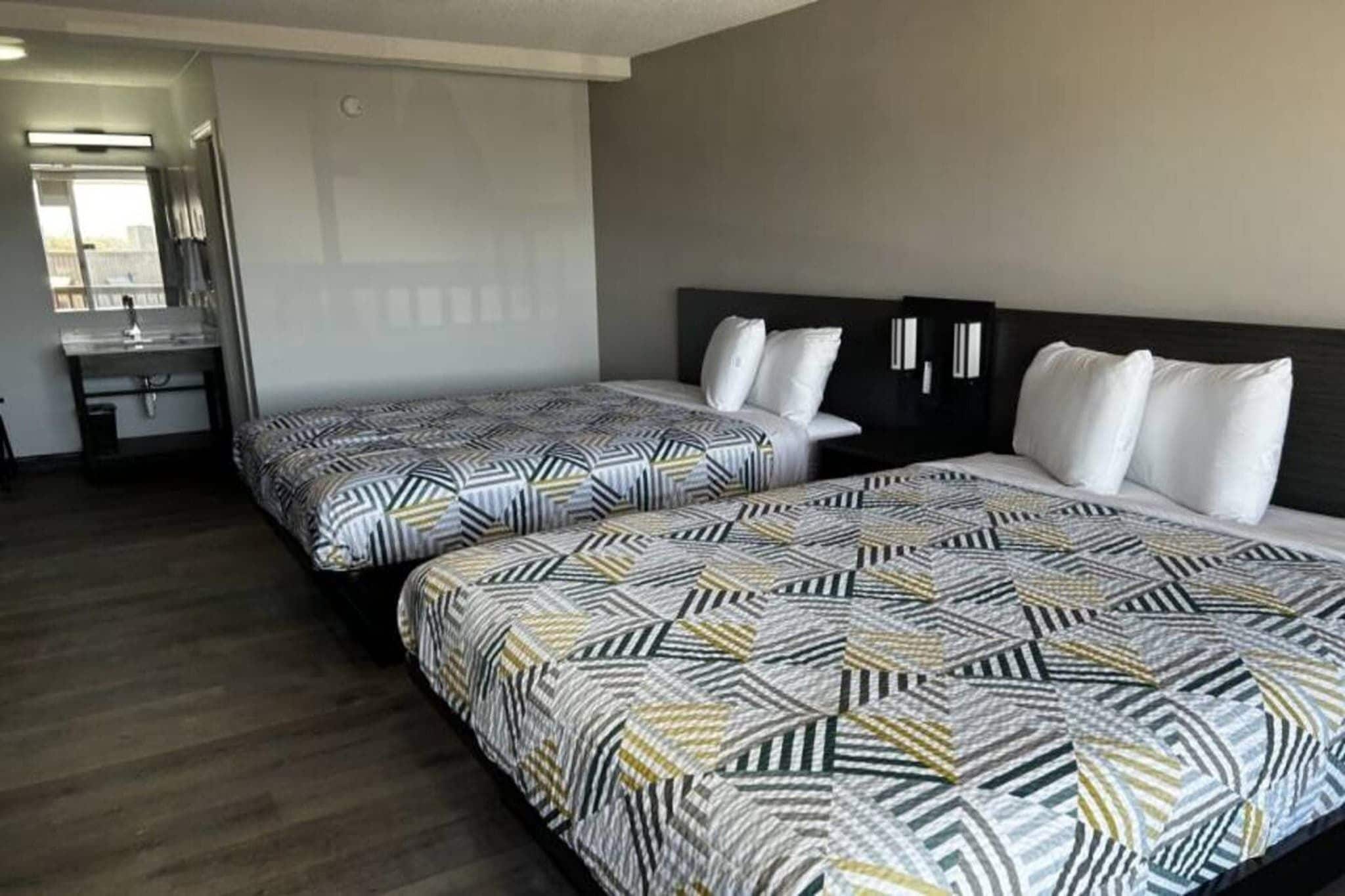 A hotel room with two beds, a bathroom, and a view of the outside.
