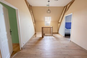 A hallway with wooden flooring, a wooden railing, and a door on the left. - Vacation Home “La Ramellerie - Grange Arthuis” with Wi-Fi and Air Conditioning (Lavau)