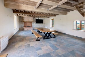 A spacious room with a large wooden table and benches, a brick fireplace, and a stone floor. - Vacation Home “La Ramellerie - Grange Arthuis” with Wi-Fi and Air Conditioning (Lavau)