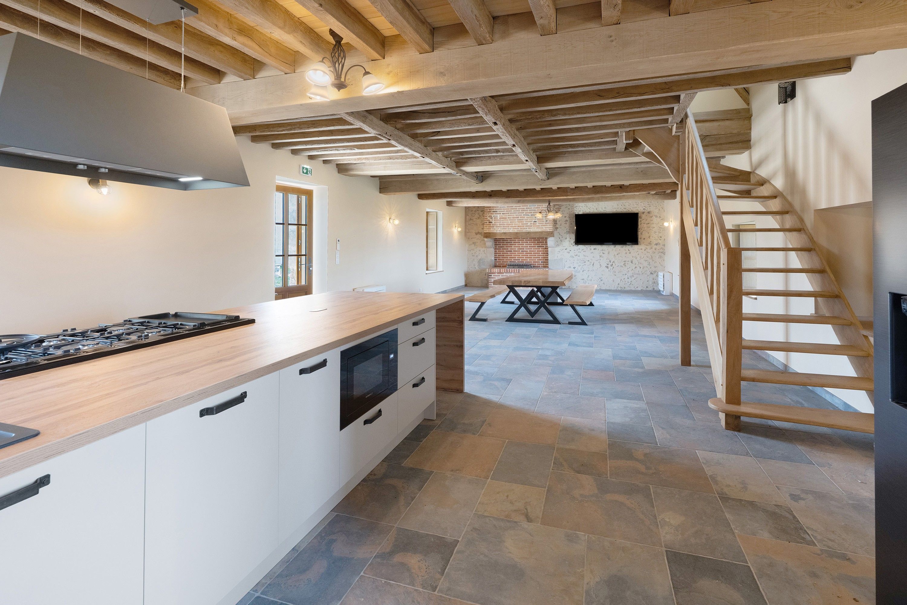 Een ruime keuken met een centraal eiland, een eethoek met tafel en banken, en een trap naar een bovenverdieping.