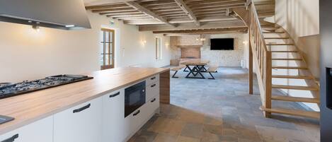 A spacious kitchen with a central island, a dining area with a table and benches, and a staircase leading to an upper level.