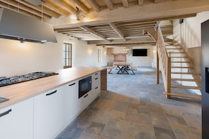 A spacious kitchen with a central island, a dining area with a table and benches, and a staircase leading to an upper level. - Vacation Home “La Ramellerie - Grange Arthuis” with Wi-Fi and Air Conditioning (Lavau)