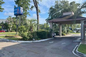 L’entrée d’un motel, avec un espace de stationnement couvert, un panneau indicateur et de la végétation environnante.