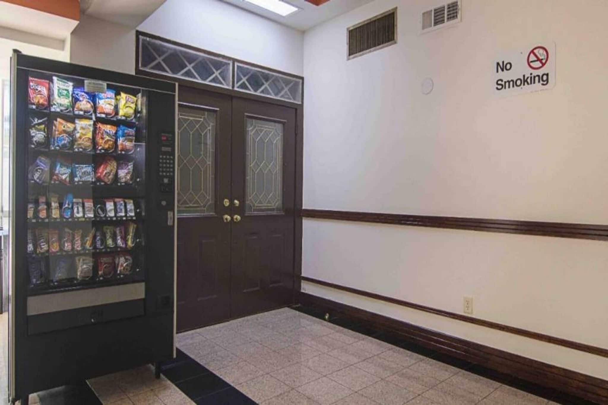 A hallway with a vending machine stocked with snacks and a 'No Smoking' sign on the wall.