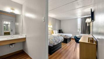 A hotel room with a wooden floor, a bed with patterned bedding, a desk with a chair, and a large mirror.