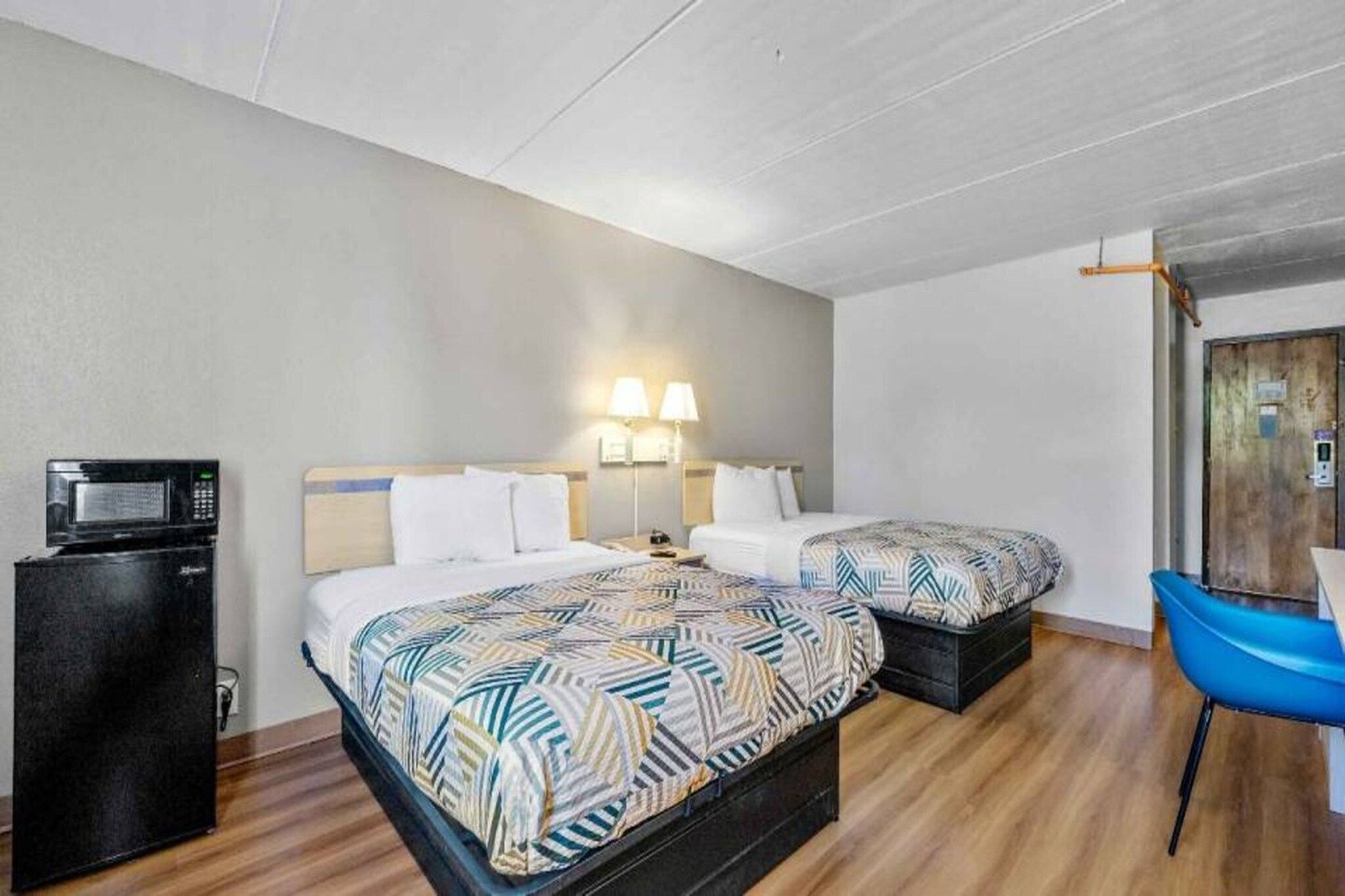 A hotel room with two beds, a desk, a chair, and a microwave.