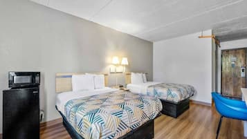A hotel room with two beds, a desk, a chair, and a microwave.