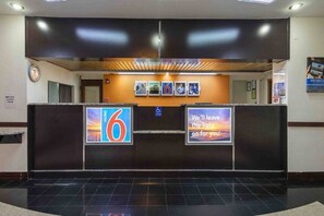 Zona de recepción de un hotel con un panel de señalización digital, un reloj y un letrero de accesibilidad para sillas de ruedas.