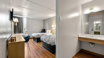 Ein Hotelzimmer mit Bett, Nachttisch, Lampe und einem Badezimmer mit Spiegel und Waschbecken.