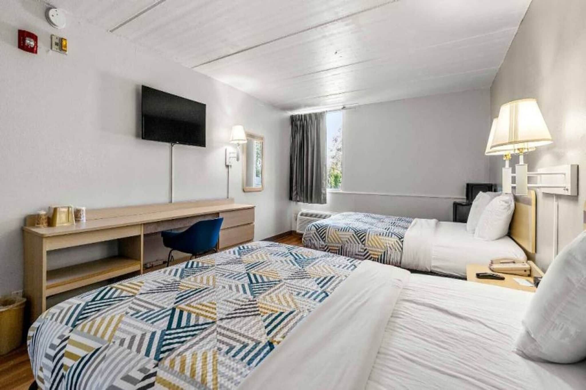 A hotel room with two beds, a desk, a chair, a TV, and a window with curtains.