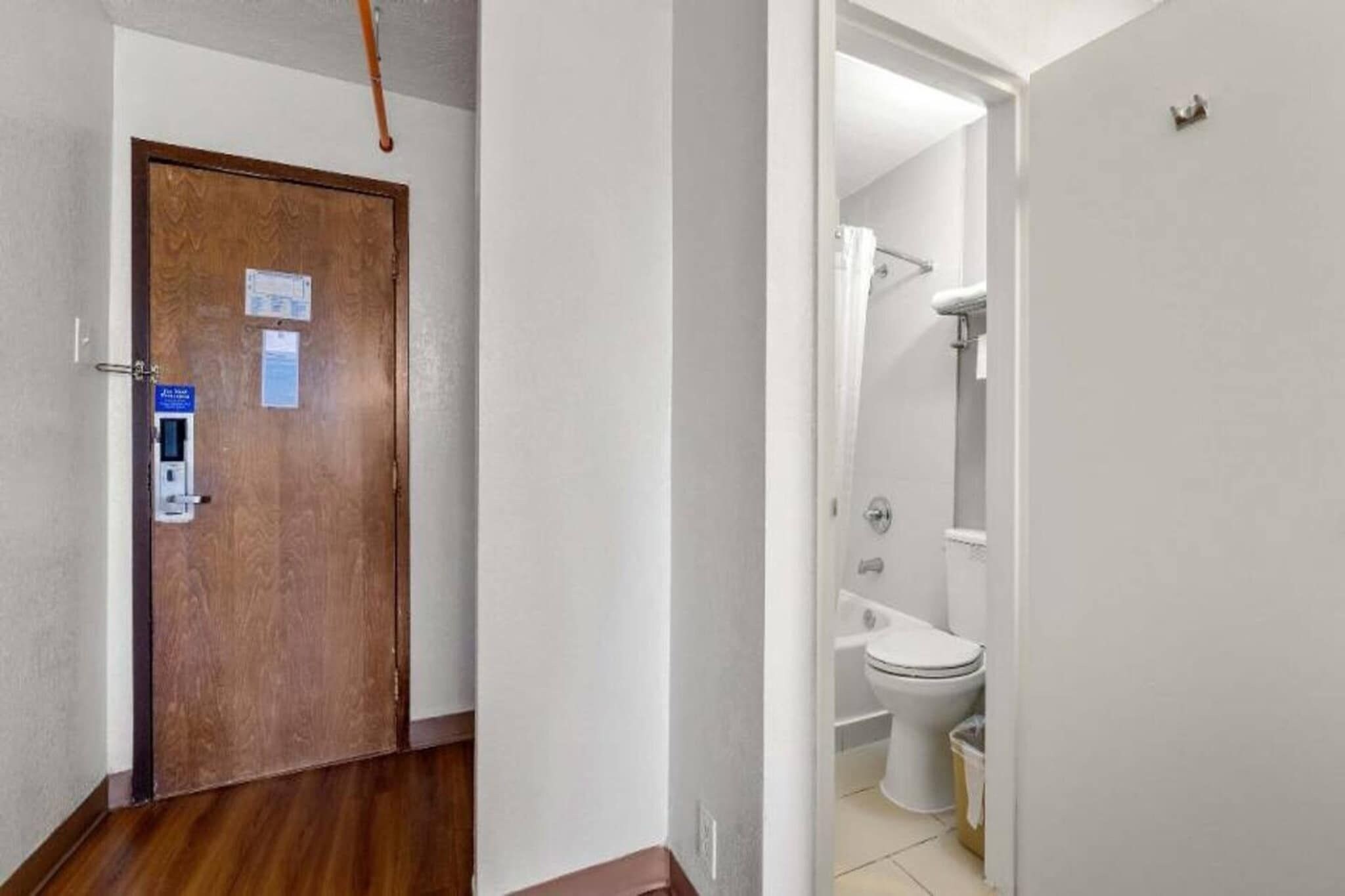 A wooden door with a blue sign, a white wall, and a glimpse of a bathroom with a toilet and shower.