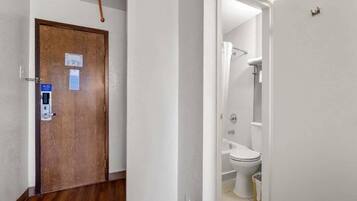 A wooden door with a blue sign, a white wall, and a glimpse of a bathroom with a toilet and shower.