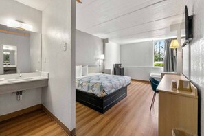 Ein modernes Hotelzimmer mit einem großen Bett, einem Schreibtisch, einem Stuhl, einem Schminktisch mit Spiegel und einem Fenster.