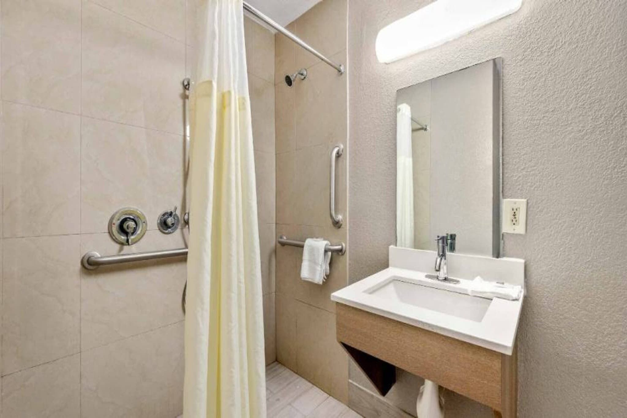 A bathroom with a shower, grab bars, a sink, and a mirror.