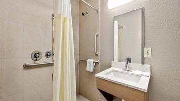 A bathroom with a shower, grab bars, a sink, and a mirror.