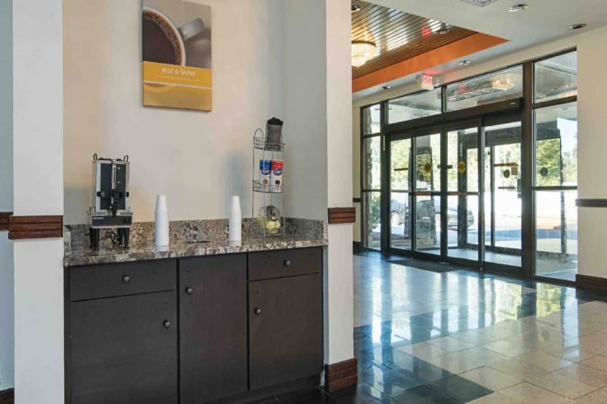 Zona de recepción con máquina de café, un bote de basura y puerta de vidrio que da al exterior.