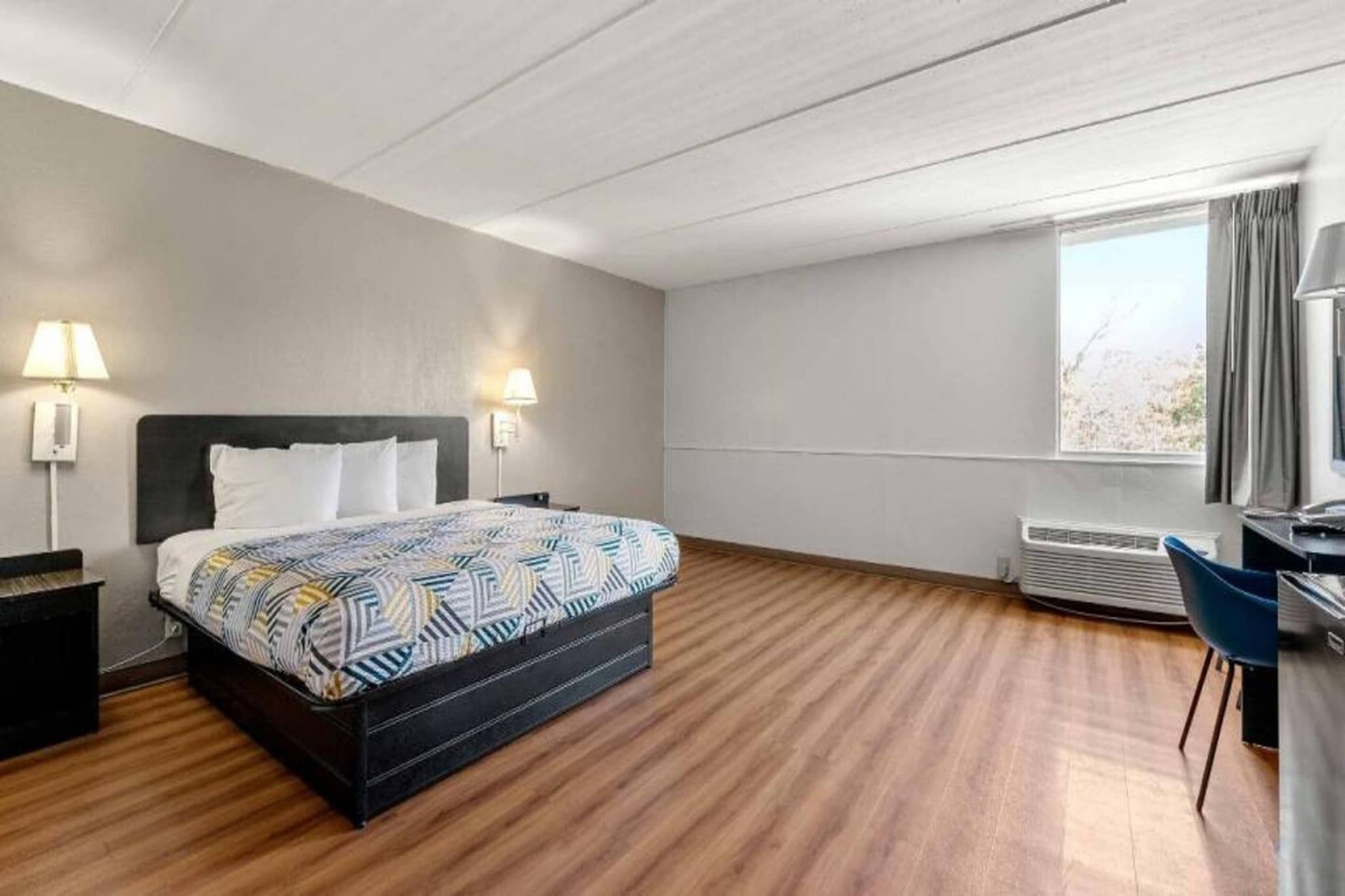 Una habitación de hotel con una cama, dos lámparas de noche, un escritorio y una ventana.