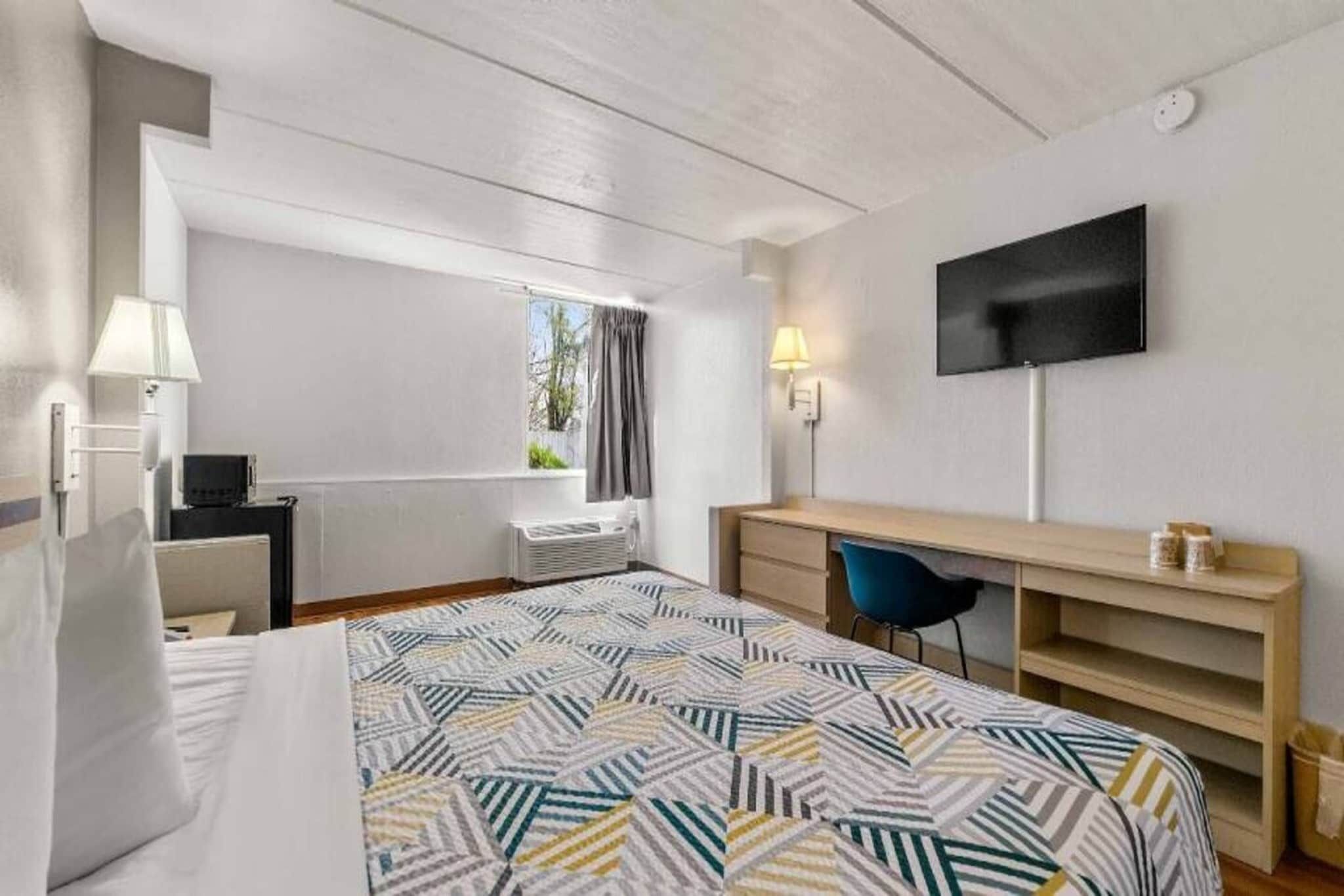 Ein Hotelzimmer mit Bett, Schreibtisch, Stuhl, Fernseher und einem Fenster mit Vorhängen.