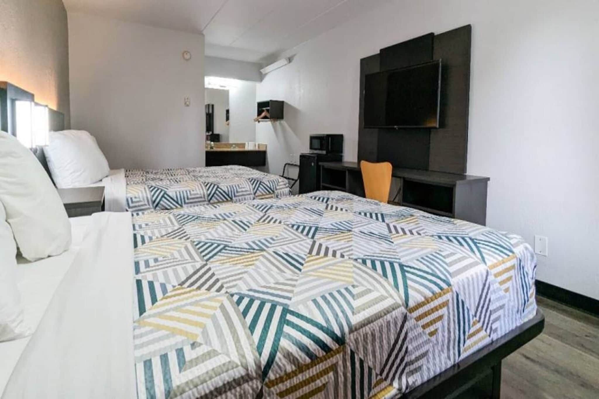 Une chambre d’hôtel avec deux lits, un bureau, une chaise, une télévision et un miroir.