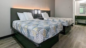 A hotel room with two beds, a nightstand, a wall-mounted TV, and a bathroom with a window. - Cozy 2-Bed Room|Free Wifi|Vending (Nashua)