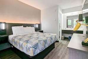 Habitación de hotel con cama, mesitas de noche, escritorio con silla, espejo y ventana.