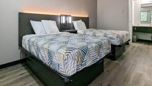 Una camera d'albergo con due letti, un comodino, una finestra e un bagno.