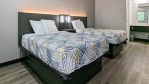 Habitación de hotel con dos camas, una mesita de noche, una ventana y un baño.