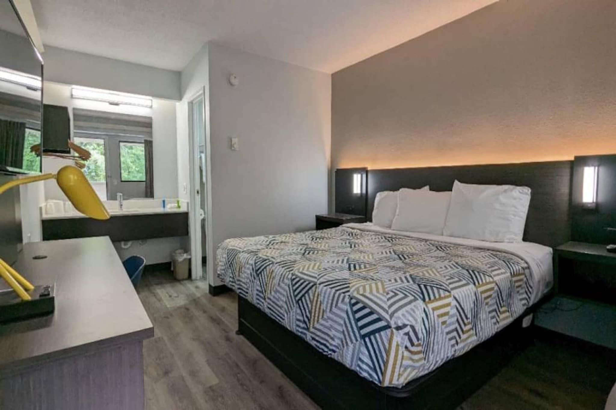 Een hotelkamer met een bed, nachtkastjes, een bureau en een spiegel.