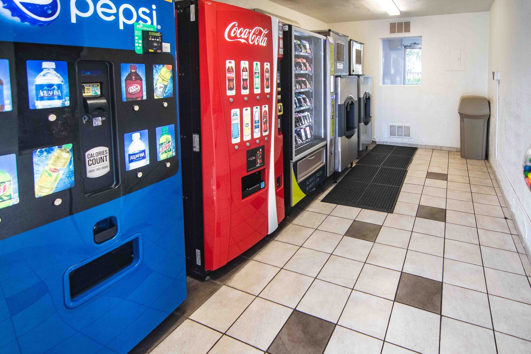Een rij automaten met diverse drankjes, waaronder Pepsi en Coca-Cola, in een betegelde ruimte.