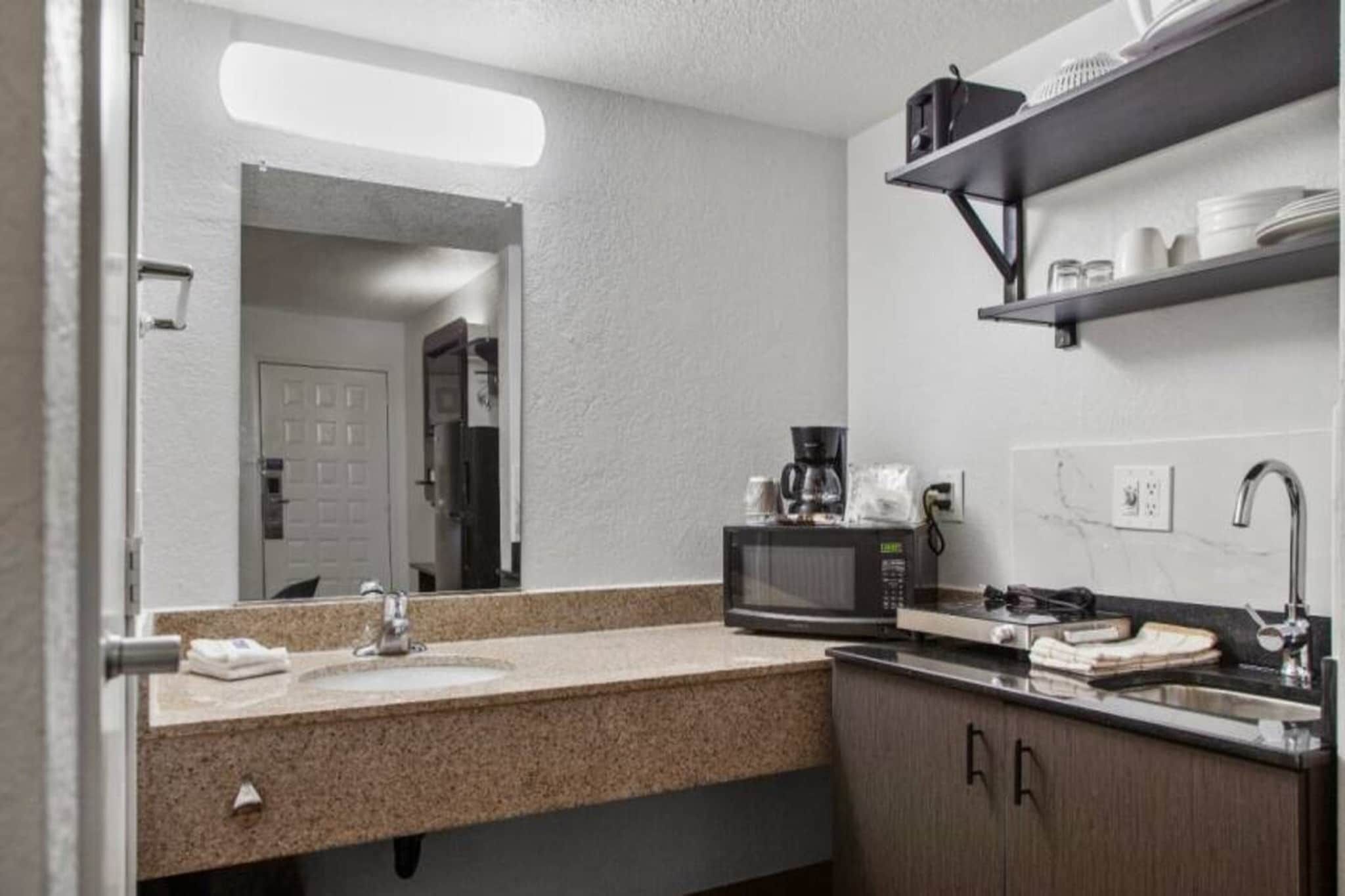 Et badeværelse på et hotel med vask, spejl, mikroovn og hylder med toiletartikler.