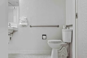 Une salle de bain équipée de toilettes, d’un lavabo, d’un porte-serviettes et d’une barre d’appui.