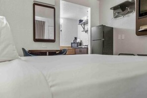 Een hotelkamer met een bed, een bureau, een spiegel, een koelkast en een magnetron.