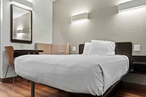 Une chambre d’hôtel avec un lit, une chaise, un bureau et un miroir.