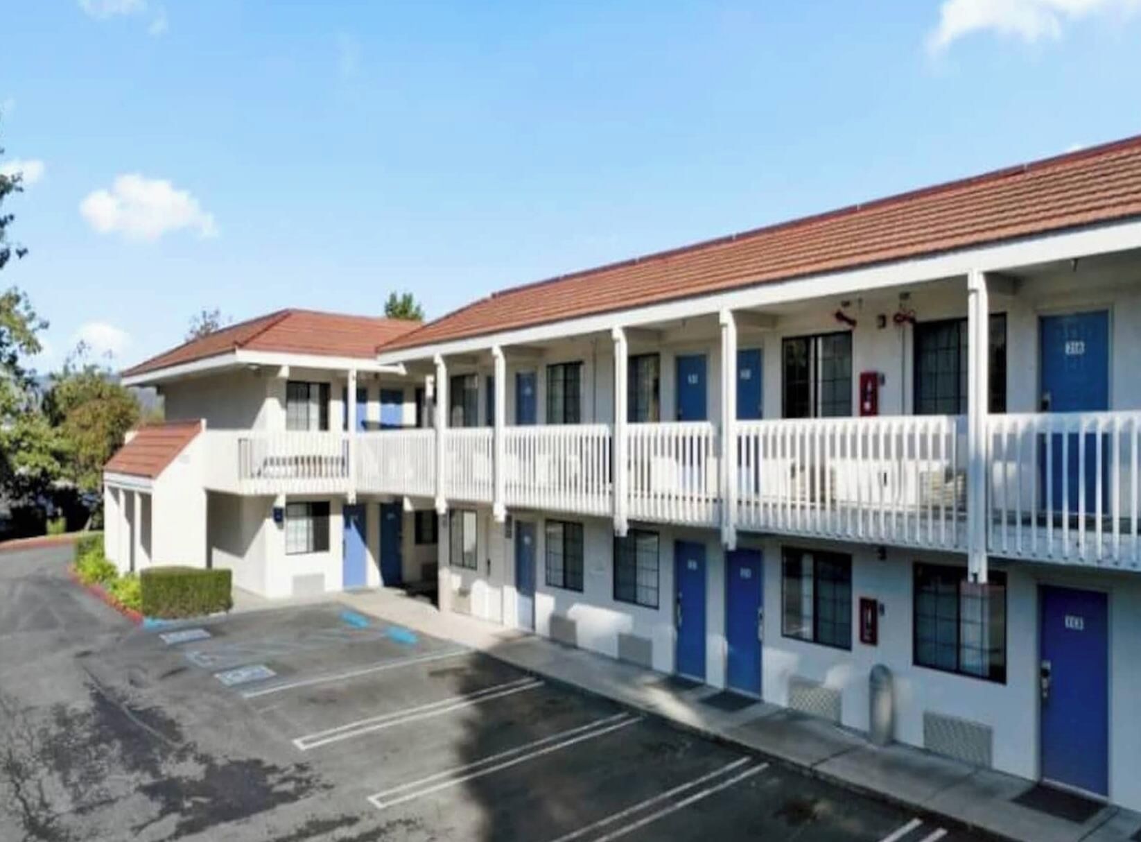 Um motel com uma fileira de quartos, cada um com uma varanda e uma porta azul.