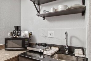 Une petite cuisine équipée d’un four à micro-ondes, d’un grille-pain, d’un évier et d’étagères au-dessus du plan de travail.