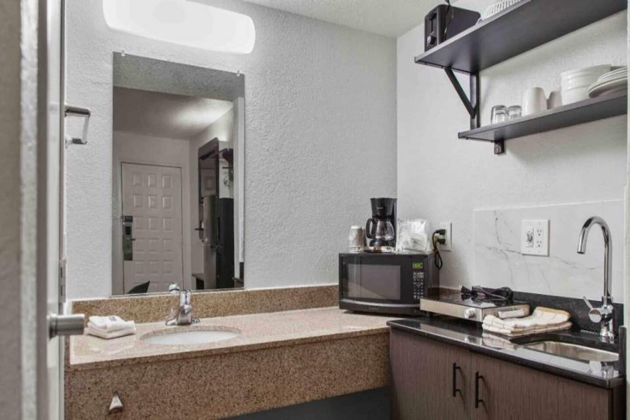 Casa de banho de hotel com lavatório, espelho, micro-ondas e uma prateleira com artigos de higiene pessoal.