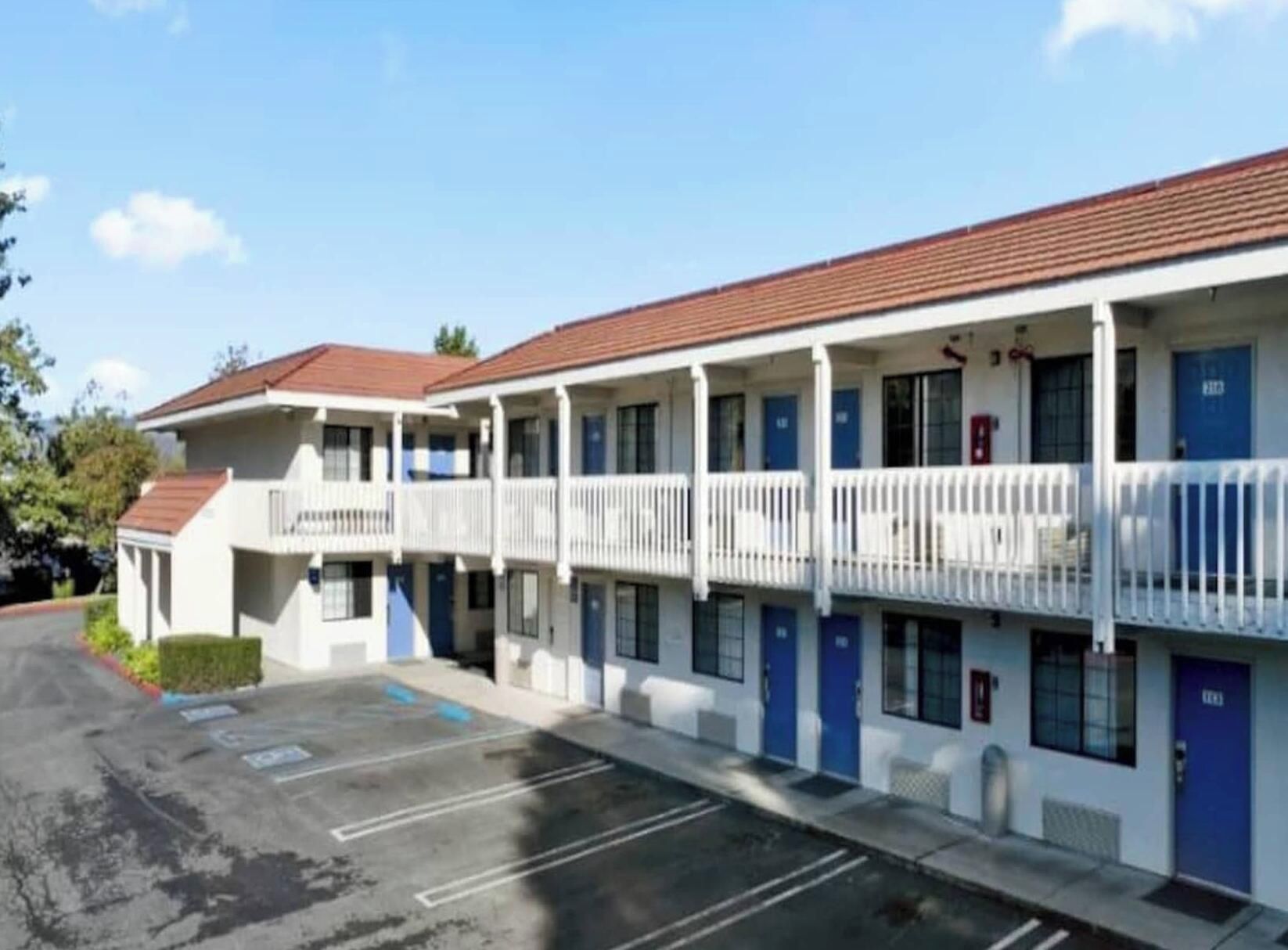 Um motel com uma fileira de quartos, cada um com uma varanda e uma porta azul.
