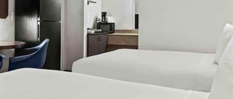 A hotel room with two beds, a small kitchenette, and a dining area with a table and chairs.