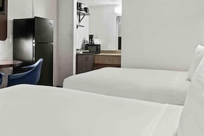 Ein Hotelzimmer mit zwei Betten, einer kleinen Küchenzeile und einem Essbereich mit Tisch und Stühlen.