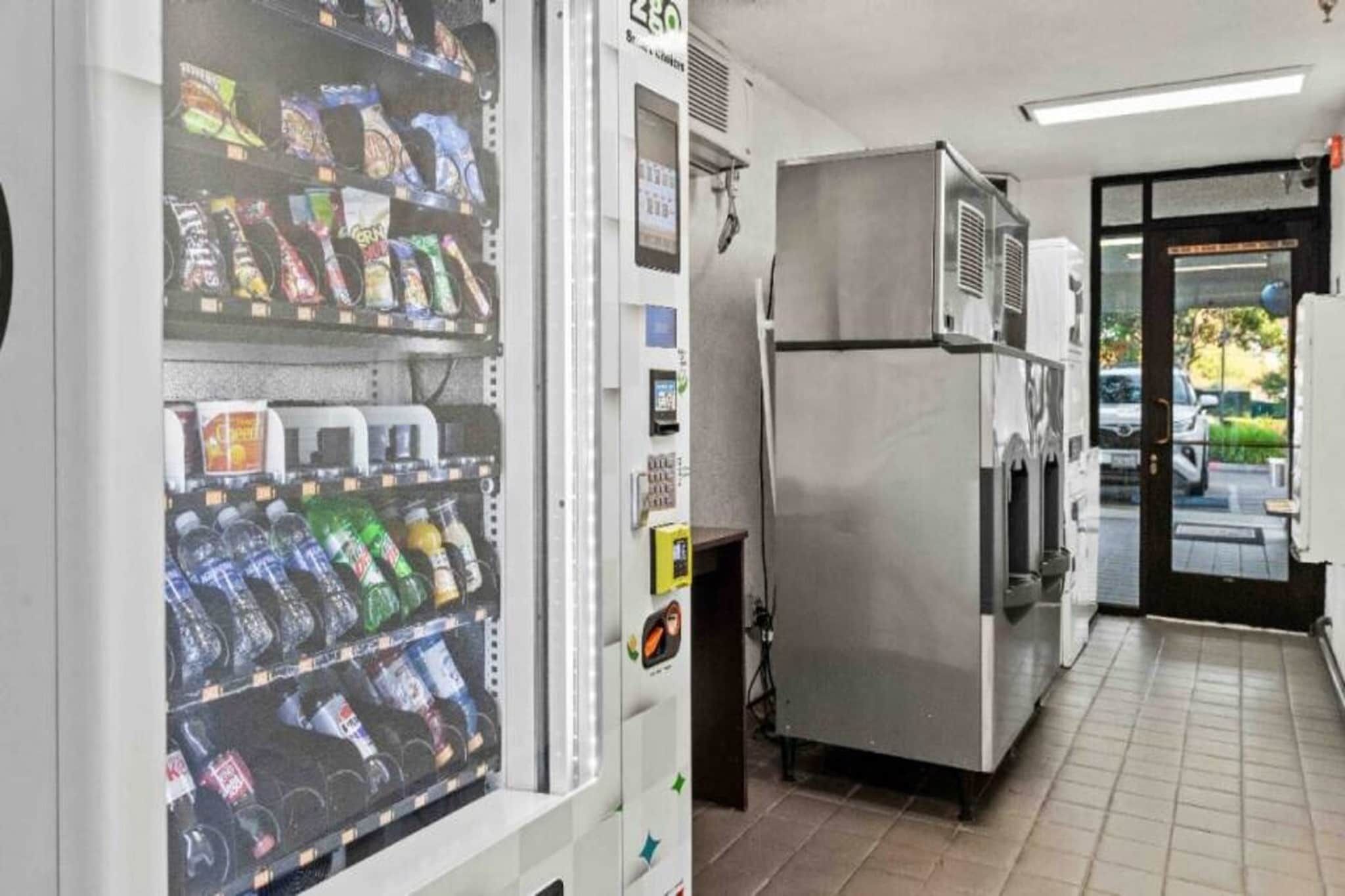 Een automaat met diverse drankjes en een koelkast in een commerciële omgeving.
