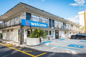 A building with a '6 Welcome' sign, a parking area with disabled parking spaces, and a black car parked in front. - 1 Full Bed | Premium, Mini Fridge (Kissimmee)