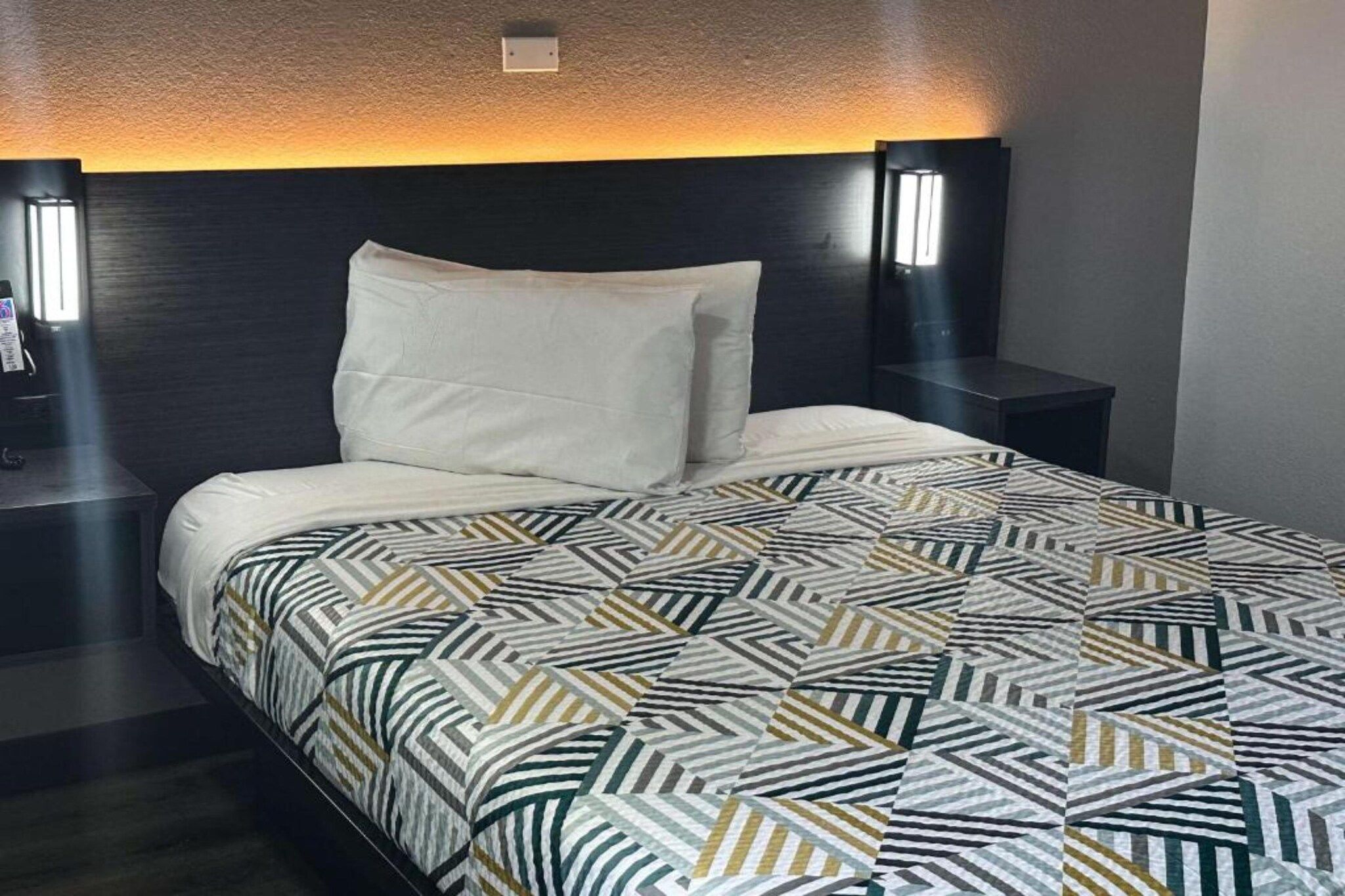 A hotel room with a bed, a nightstand, and a wall-mounted lamp.