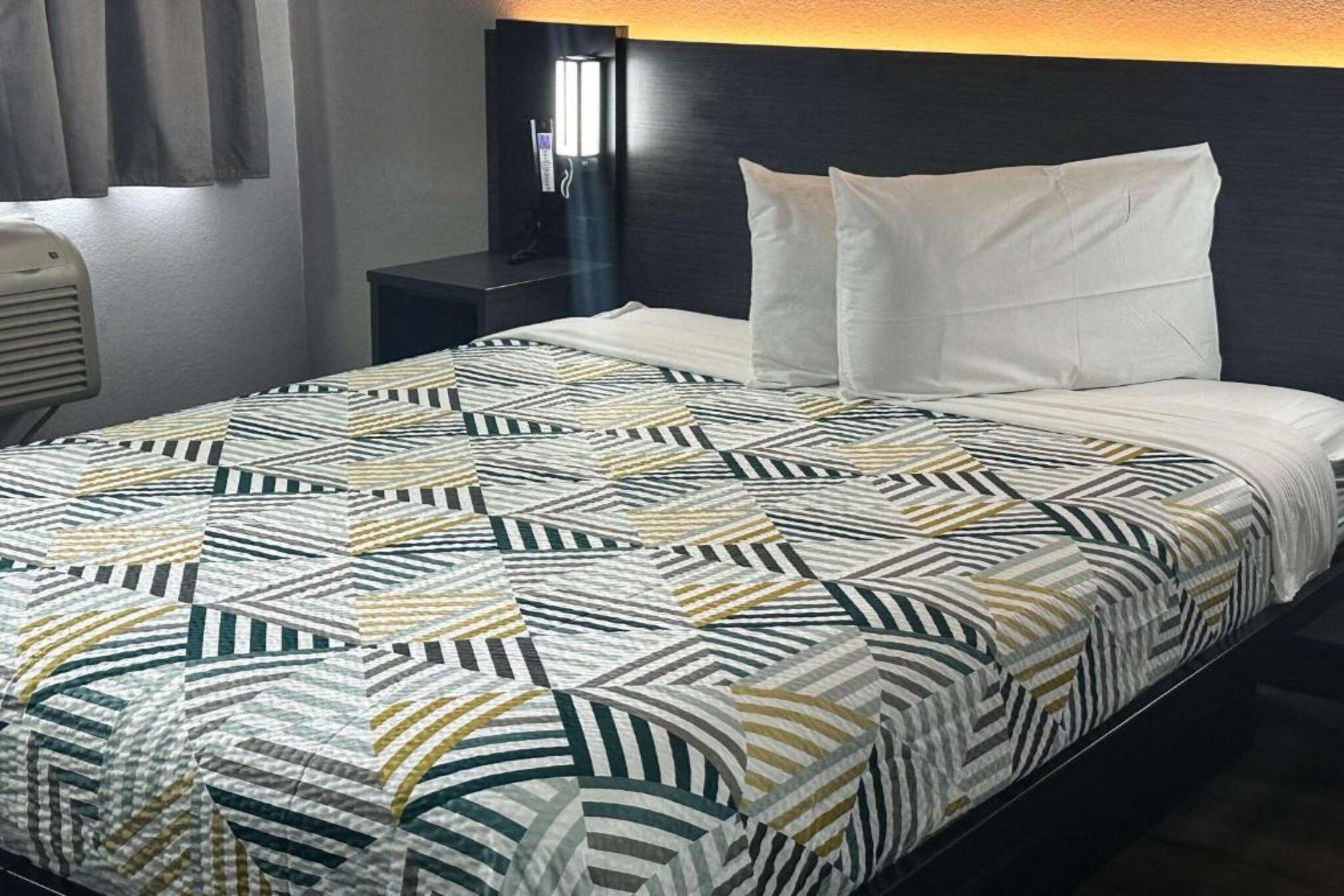 A hotel room with a bed, a nightstand, and a lamp.