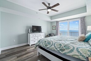 A bedroom with a bed, a TV on a dresser, a ceiling fan, and a view of the ocean. - Spacious 3BR/3BA oceanfront condo in Daytona Beach Shores. Sleeps 8 with beautiful ocean views, a large private balcony, heated oceanfront pool and direct beach access. (Daytona Beach Shores)
