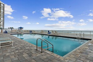 A swimming pool with a metal railing, lounge chairs, and a view of the ocean. - Spacious 3BR/3BA oceanfront condo in Daytona Beach Shores. Sleeps 8 with beautiful ocean views, a large private balcony, heated oceanfront pool and direct beach access. (Daytona Beach Shores)