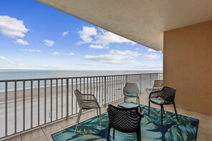 A balcony with a view of the beach, two wicker chairs, a small table, and a patterned rug. - Spacious 3BR/3BA oceanfront condo in Daytona Beach Shores. Sleeps 8 with beautiful ocean views, a large private balcony, heated oceanfront pool and direct beach access. (Daytona Beach Shores)
