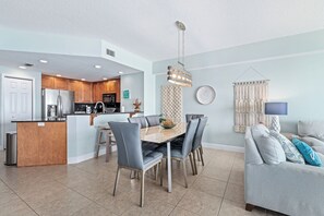 Una cocina moderna con una isla central, comedor con sillas y sala de estar con sofá y lámpara.