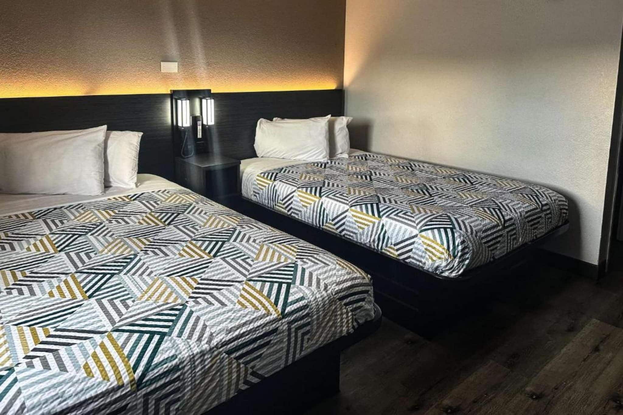 Two twin beds with geometric patterned bedding, a wall-mounted nightstand, and a wall-mounted light fixture.