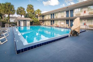 A swimming pool with lounge chairs and a covered area, surrounded by a building with multiple windows and balconies. - 2 Full Beds | Premium, Mini Fridge (Kissimmee)