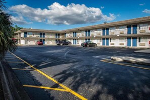 A motel with a parking lot, multiple vehicles, and a clear sky. - ADA Full Bed|Tub|Micfridge (Kissimmee)